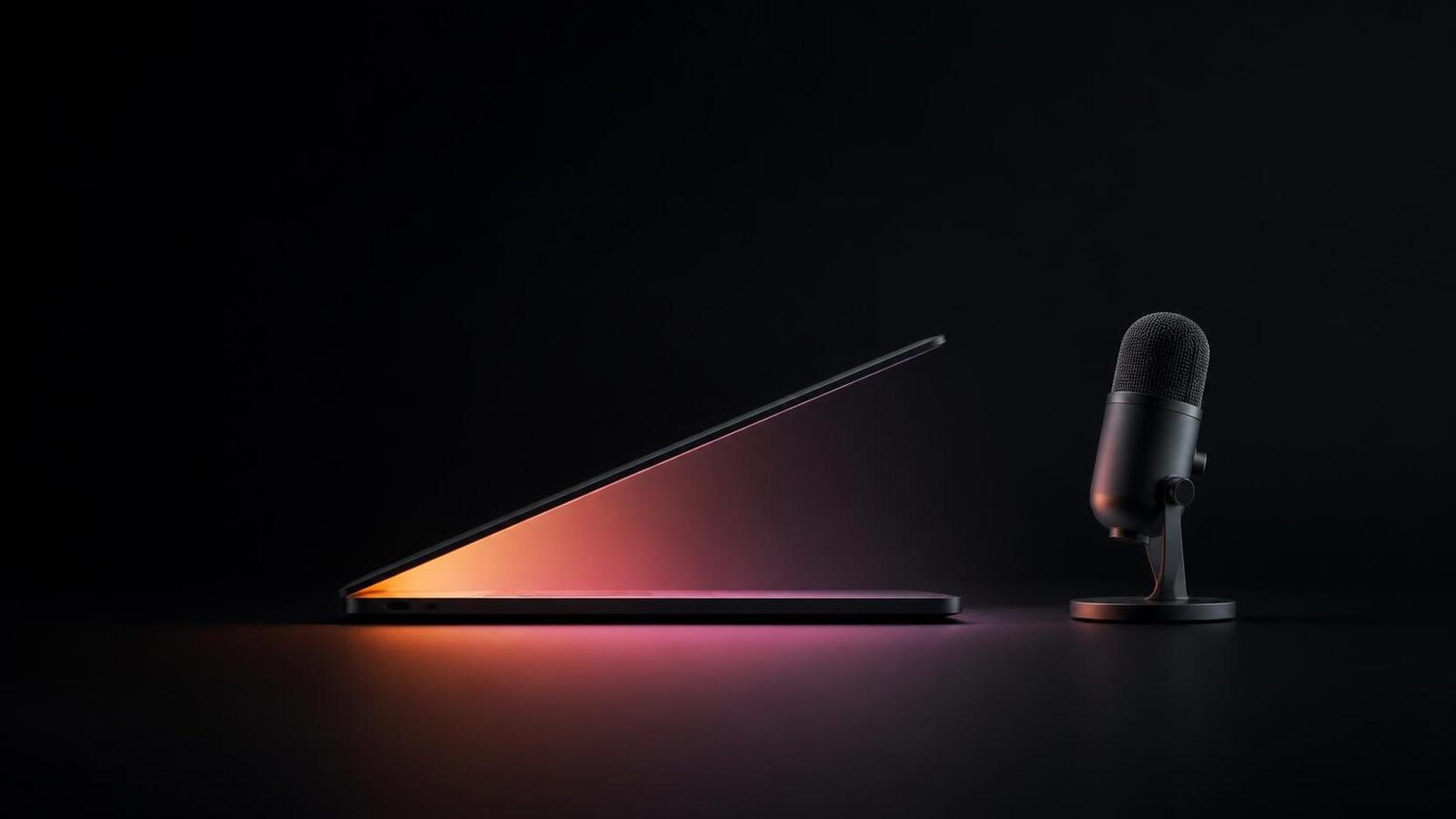 A thin dark laptop seen in profile, its lid nearly closed, with warm amber-to-magenta light spilling from the gap onto a black surface, and a graphite microphone standing beside it.